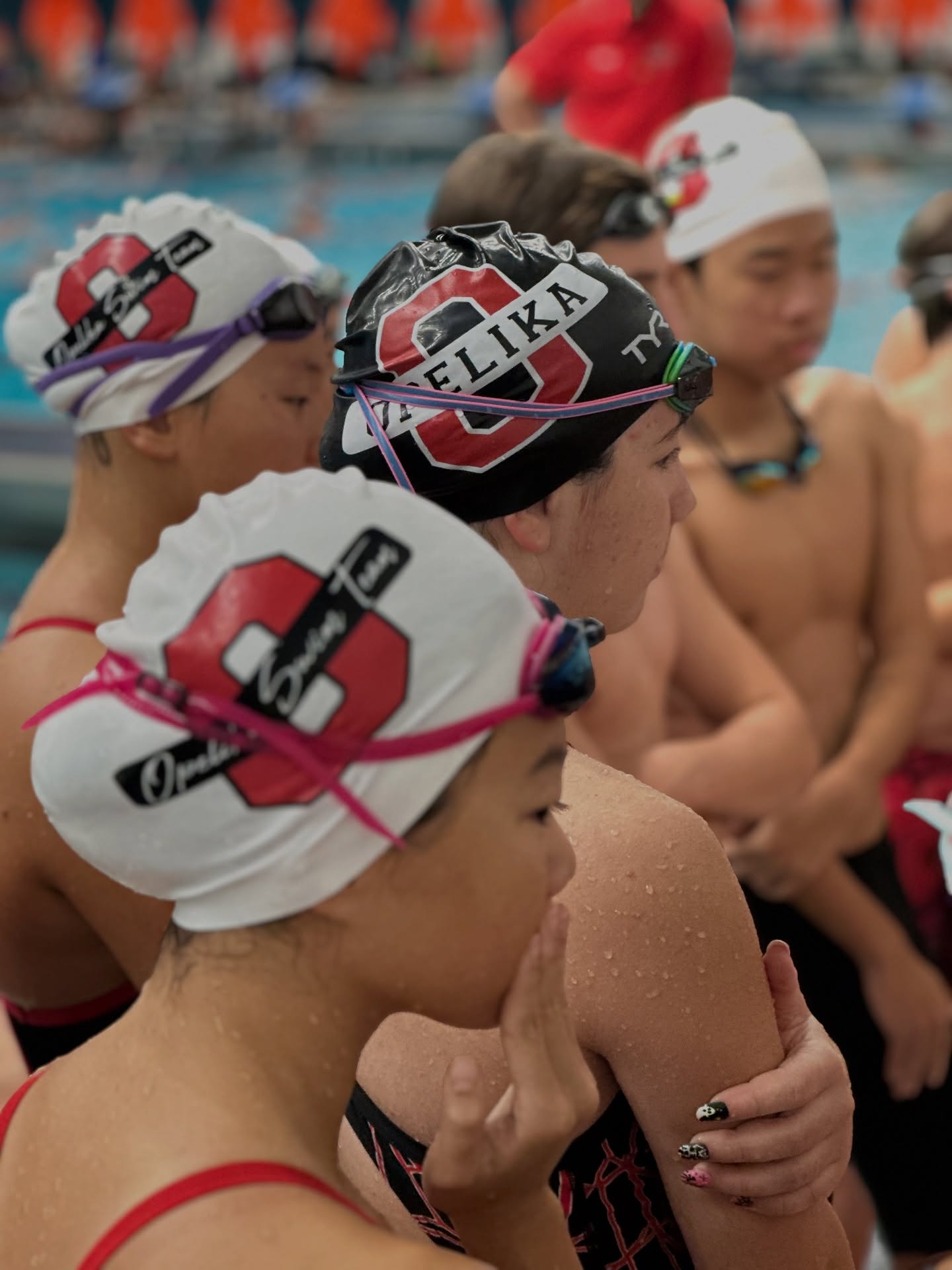 Swimmers racing with a swim meet scoreboard and officials on deck